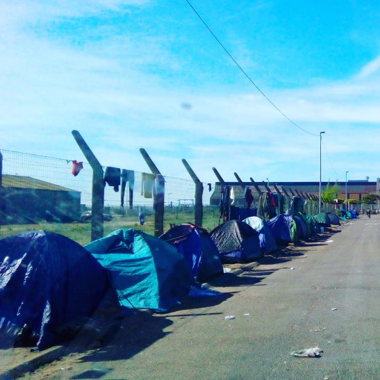 Image shows tents against a fence and a blue sky